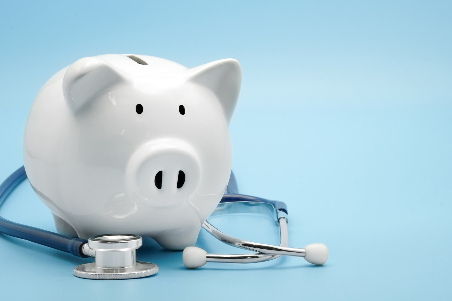 Une tirelire et un stetoscope sur un fond blanc intégrant l'idée d'économies sur les dépenses de santé.